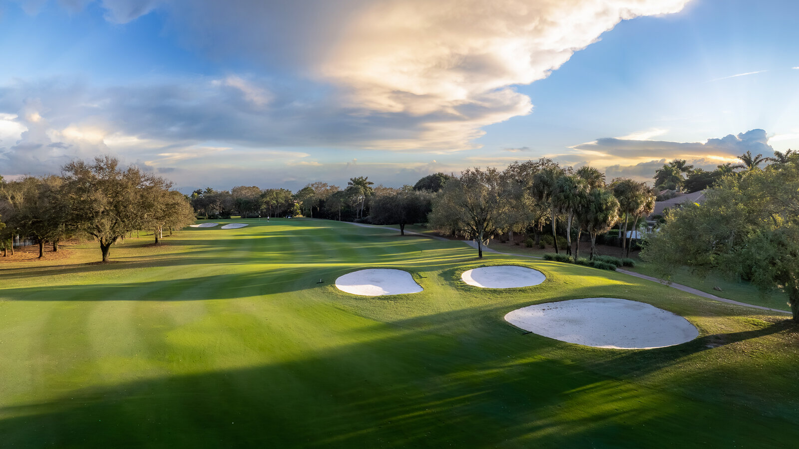 Aerial of a golf course fairway with a post-sunset sky composited in