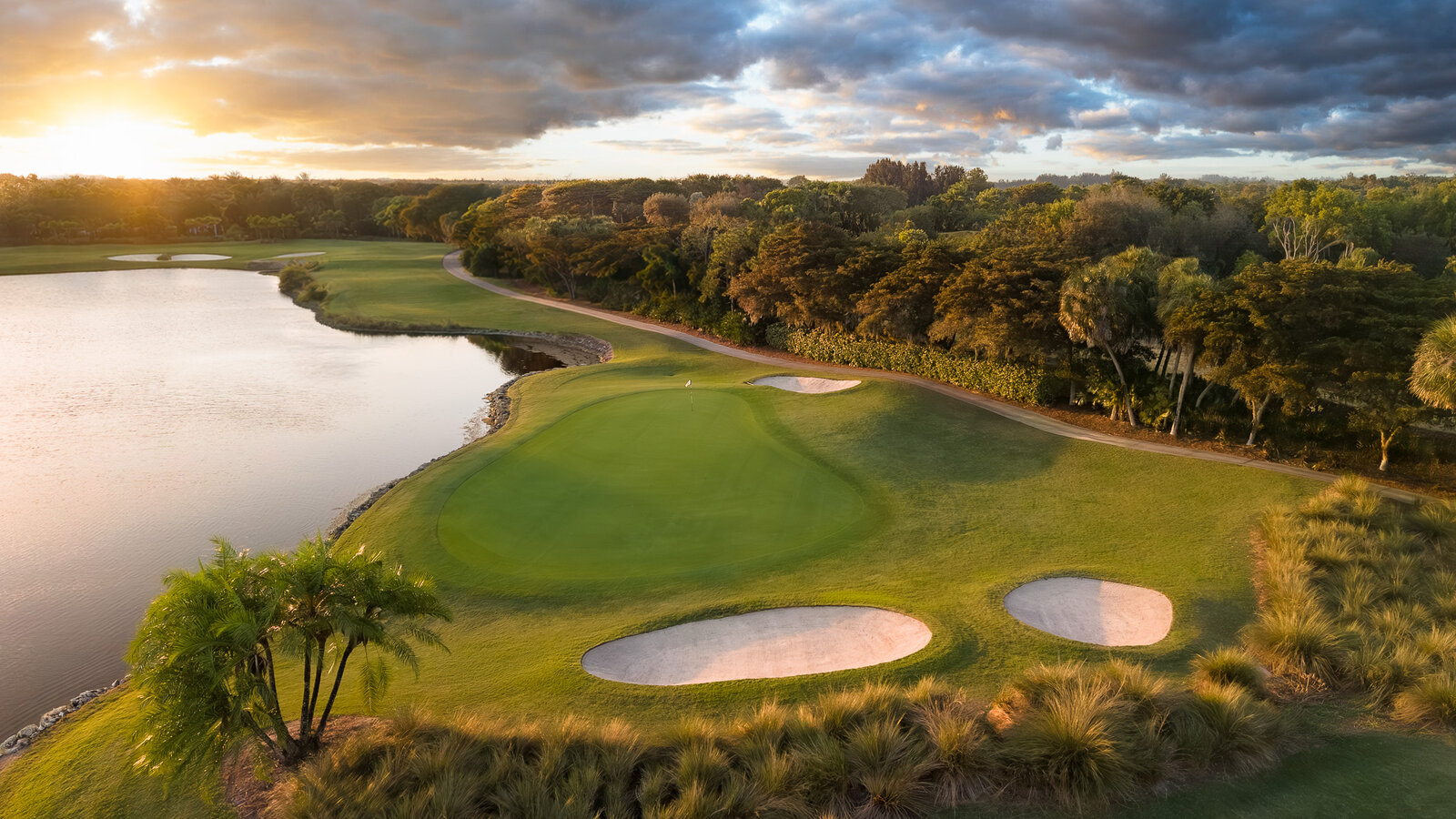 Aerial of a golf course and lake with a dramatic golden-hour sunset composited in