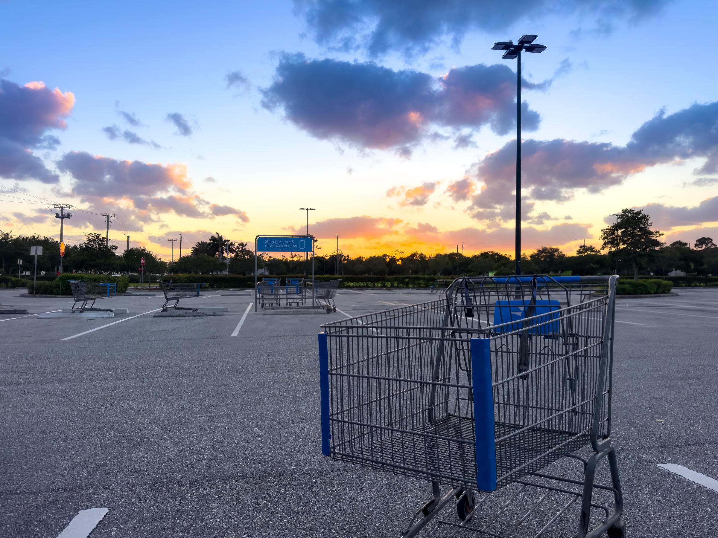 Empty grocery-store parking lot at dusk with an abandoned shopping cart and a pastel sunset — the photograph every photographer has accidentally taken.